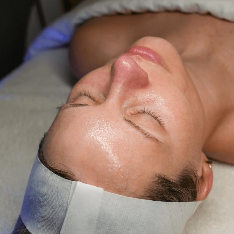 A woman with closed eyes and a white headband rests on a white surface, with a soft blue light illuminating the background.