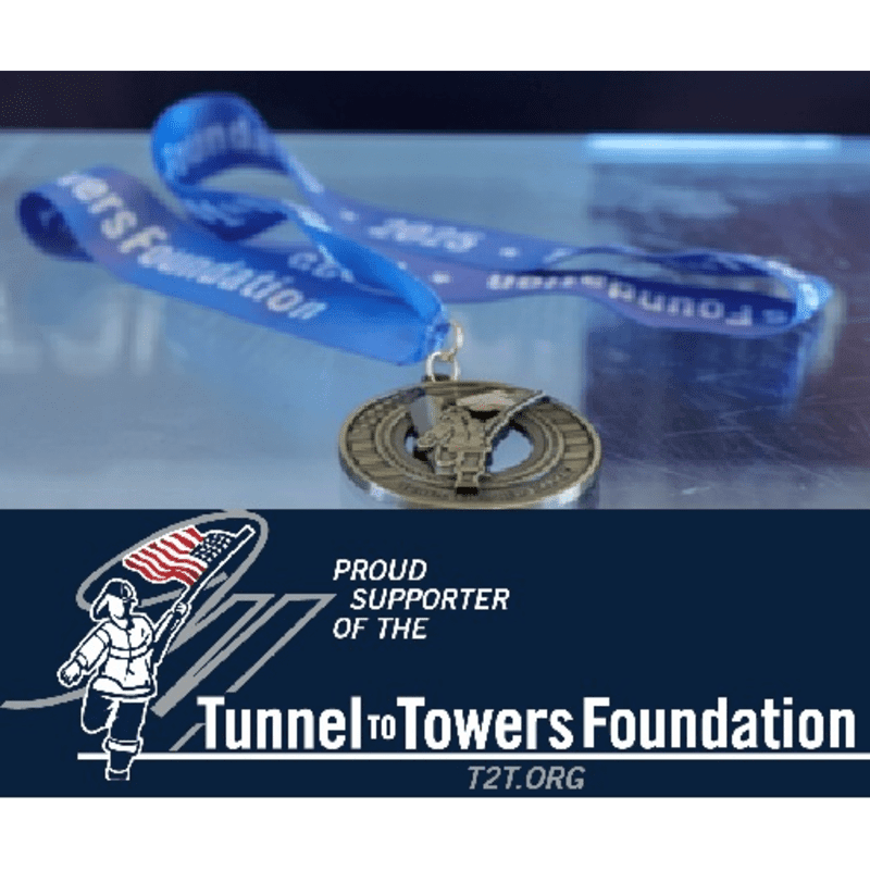 A medal with a blue ribbon lies on a reflective surface in the foreground, with a dark blue banner featuring the Tunnel to Towers Foundation logo and text in the background.
