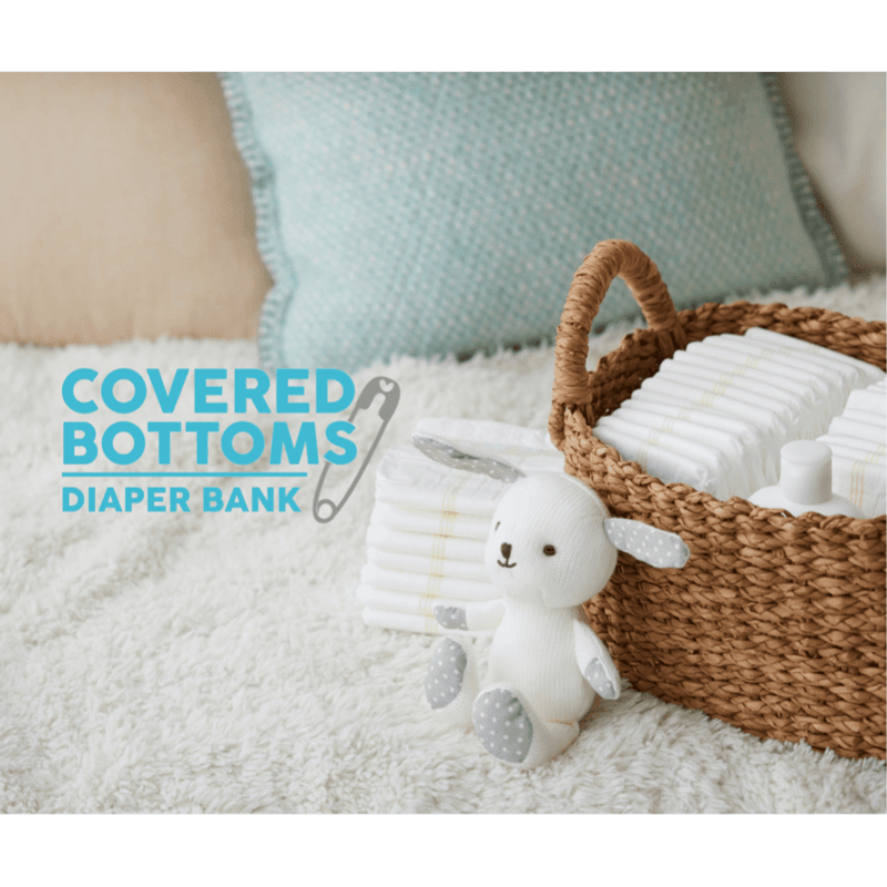 A woven basket filled with diapers sits on a fluffy white rug in the foreground, with soft pillows in the background.