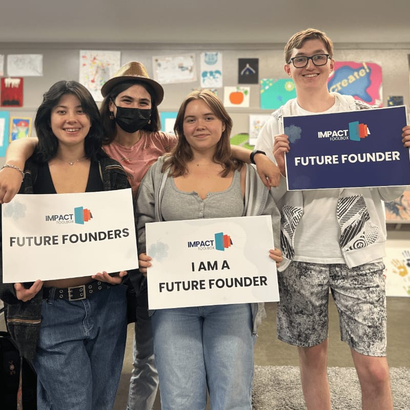 Four young people stand in the foreground holding signs that say "FUTURE FOUNDERS" and "I AM A FUTURE FOUNDER," with colorful artwork displayed on the wall in the background.