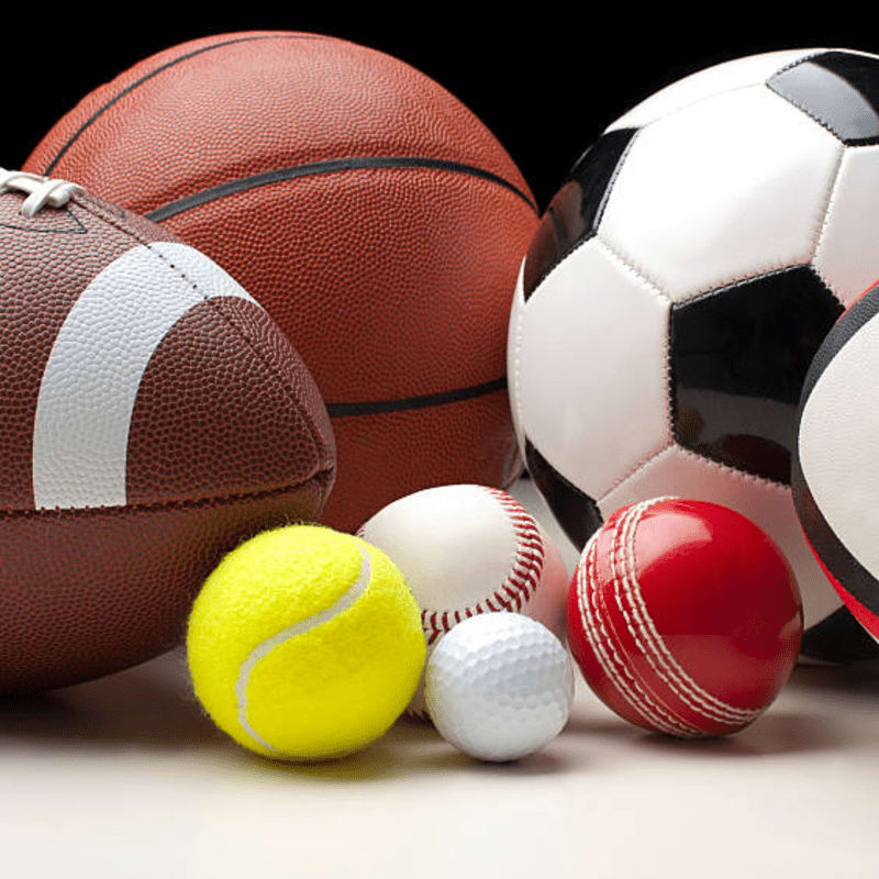 A collection of sports balls, including a football, basketball, soccer ball, tennis ball, baseball, golf ball, and cricket ball, are arranged in the foreground against a black background.