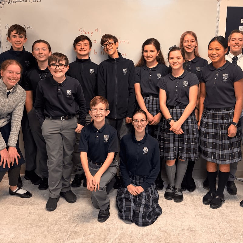 A group of students in uniform pose in front of a whiteboard with writing on it.