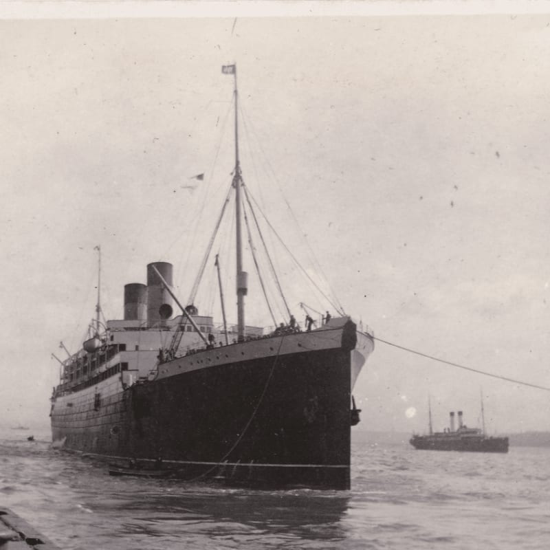 A large ocean liner dominates the foreground, with a smaller ship visible in the hazy background.