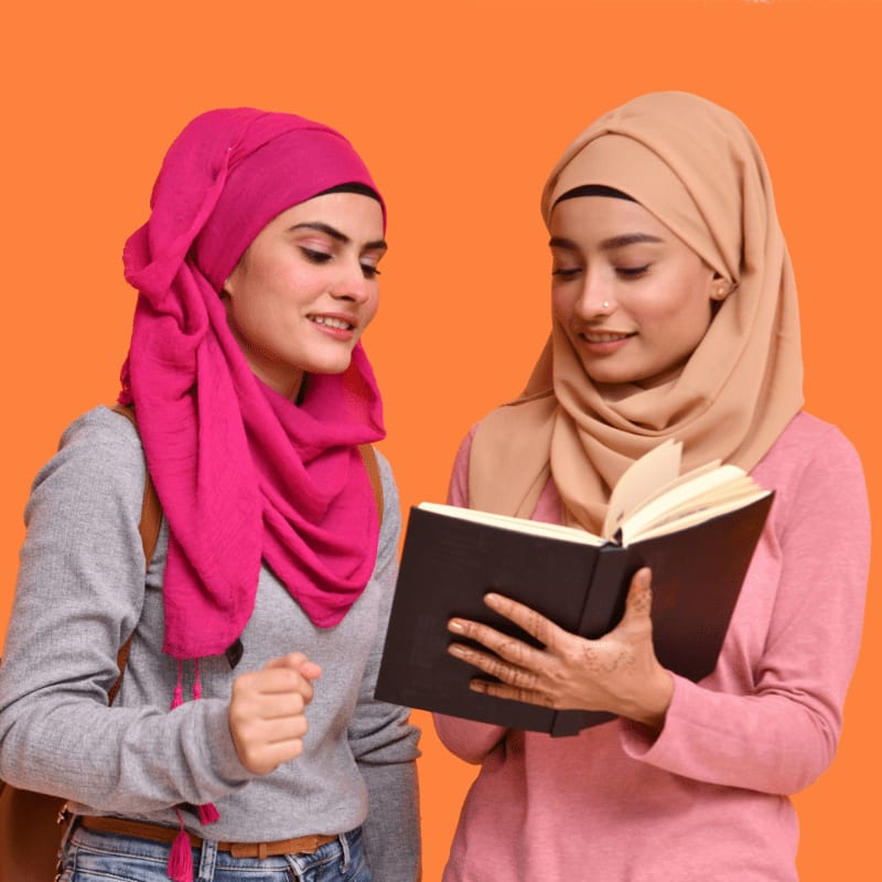 two women in hijabs are reading a book