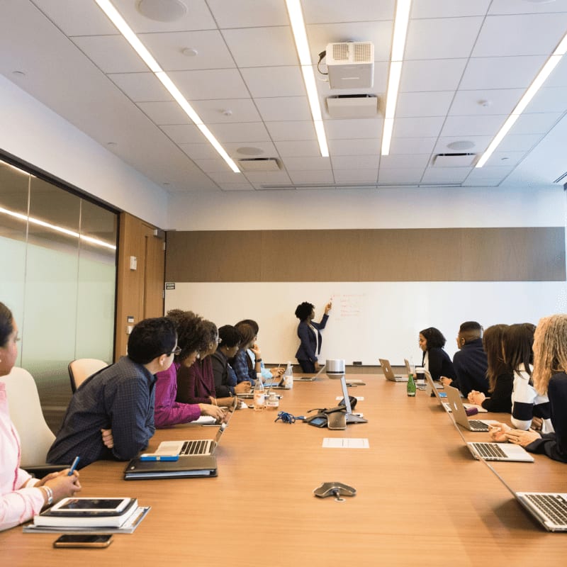 people on conference table looking at talking woman