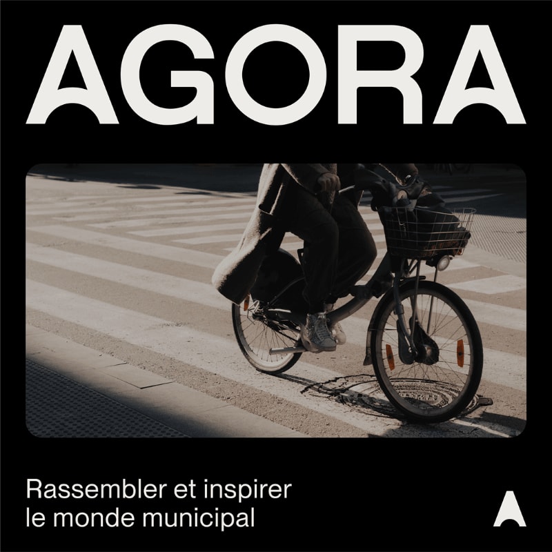 A person on a bicycle crosses a crosswalk in the foreground, with the word "AGORA" in large white letters at the top and French text at the bottom.