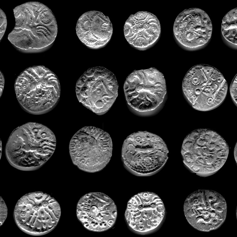 Rows of ancient, intricately designed silver coins with varied patterns are displayed against a stark black background.