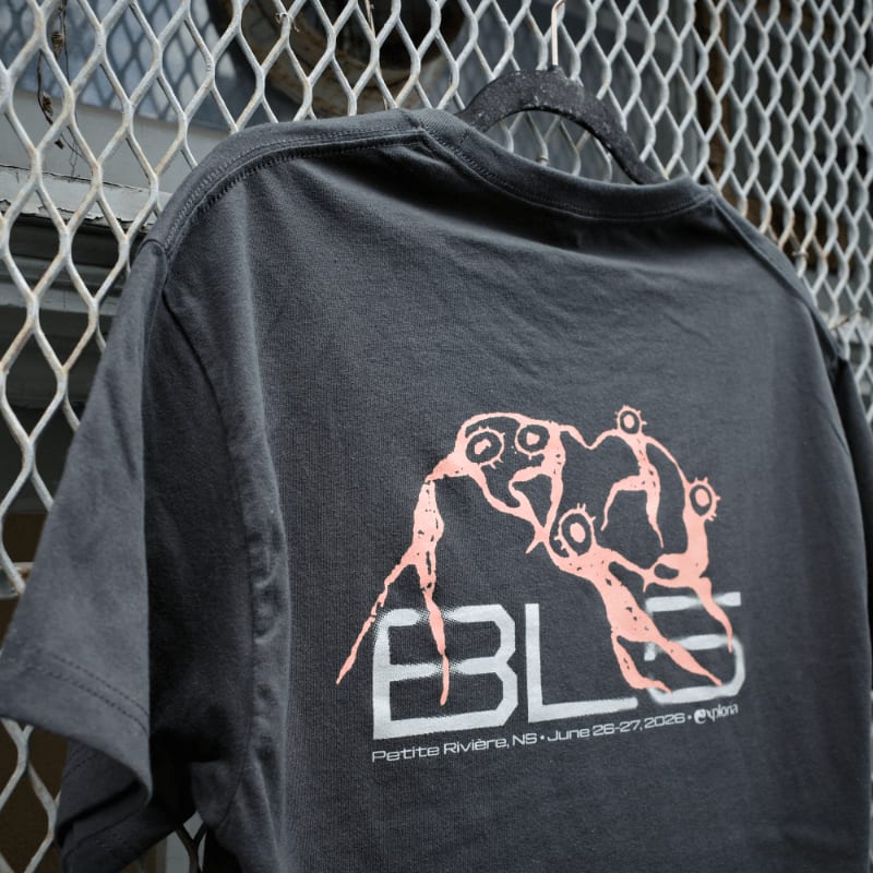 A dark t-shirt with a pink graphic and text is hanging on a black hanger in front of a metal grate.