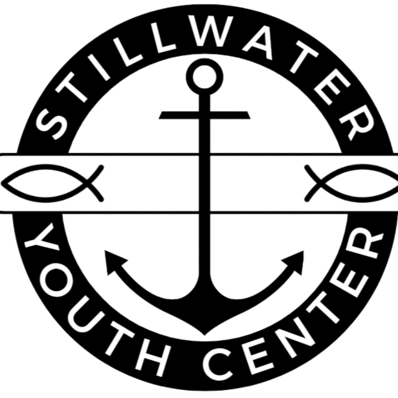 A black and white circular logo features an anchor in the foreground, with the words "STILLWATER YOUTH CENTER" encircling it, and two fish symbols on a horizontal band in the background.