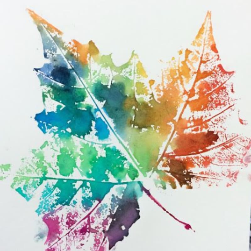 A vibrant watercolor leaf print with a rainbow of colors dominates the foreground against a plain white background.