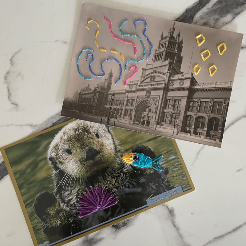 A sea otter with embroidered embellishments floats in the foreground, while a vintage building with embroidered abstract shapes is in the background.