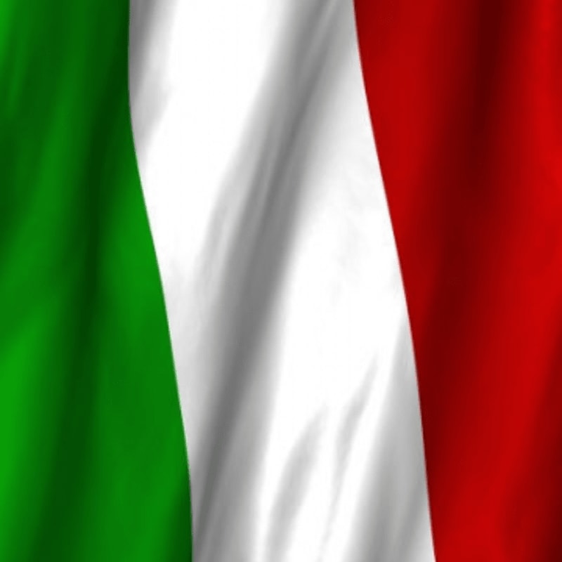 A close-up of the Italian flag, with its green, white, and red stripes rippling in the foreground against a blurred background.