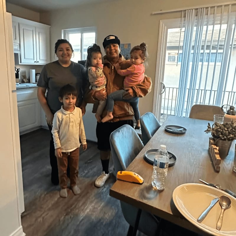 A family of five poses for a photo in a kitchen with a dining table set for a meal in the foreground.
