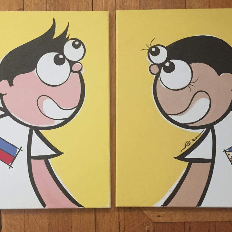 Two cartoon children with large eyes and wide smiles, each wearing a shirt with a flag, are painted on yellow canvases against a wooden background.