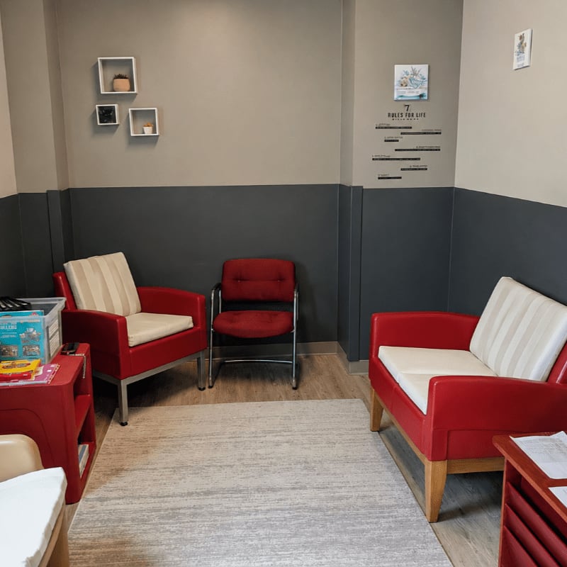Two red armchairs with striped cushions sit on a light rug in the foreground, while a dark gray accent wall with framed art and text adorns the background.