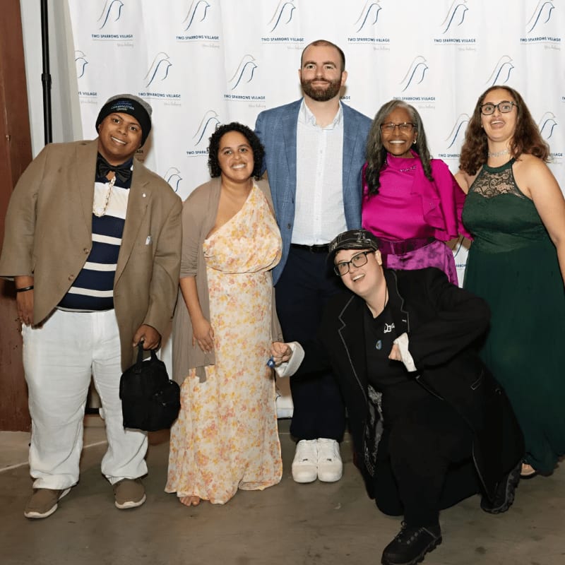 Six people pose for a photo in front of a backdrop with a logo.
