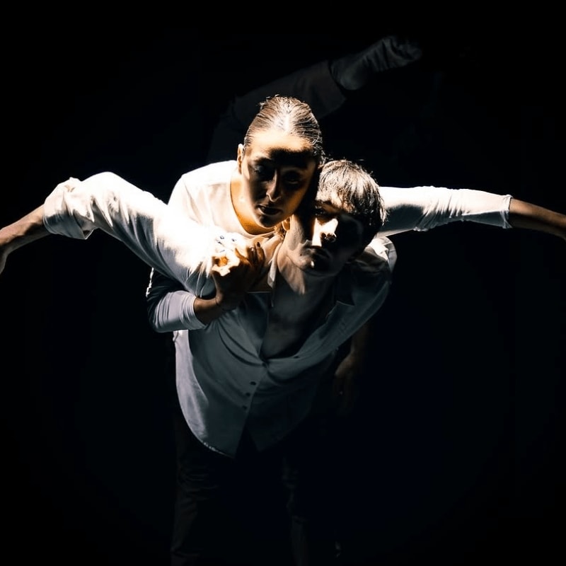 A man supports a woman in a dramatic dance pose against a stark black background.