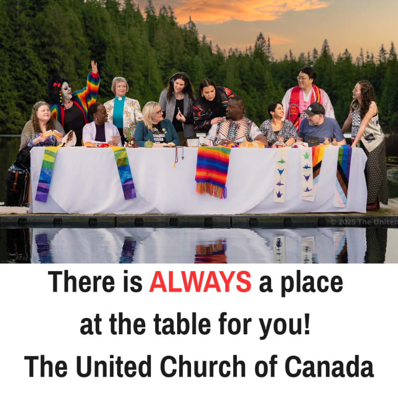 A diverse group of people are gathered around a long table set on a dock, with a lush, tree-covered hillside and a sunset in the background.