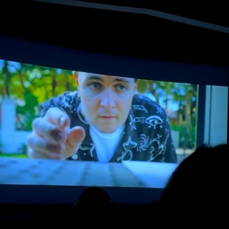 A man in a patterned shirt reaches forward towards a keyboard, with a blurred outdoor scene in the background.