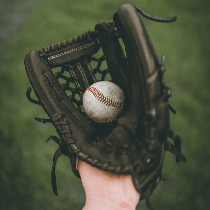 person holding baseball ball in black leather baseball mitt