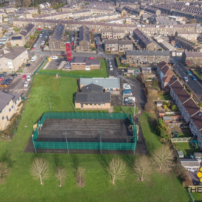 A fenced-in sports court with bare trees in the foreground is surrounded by a residential neighborhood with houses and streets in the background.