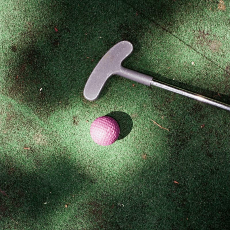Mini golf club and ball on green turf.