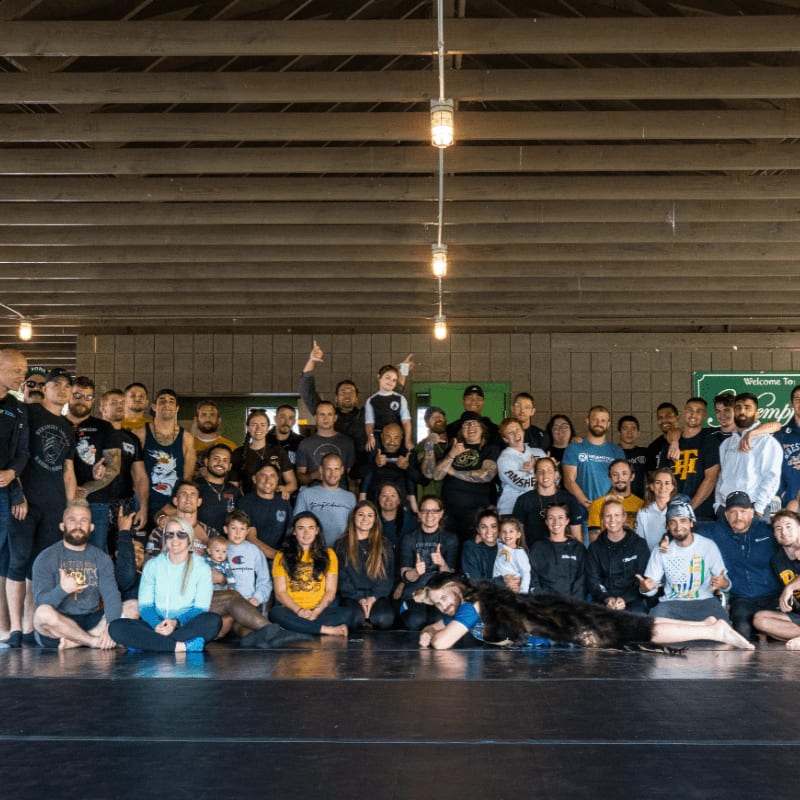 A large group of people pose for a photo on a mat in the foreground, with a building's interior and a sign in the background.
