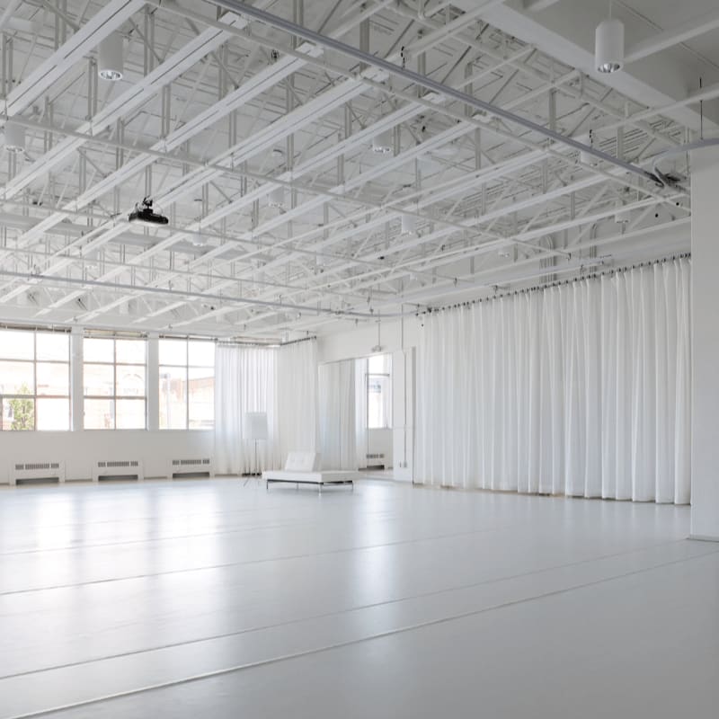 A vast, white studio space with a polished floor in the foreground and large windows and white curtains in the background.