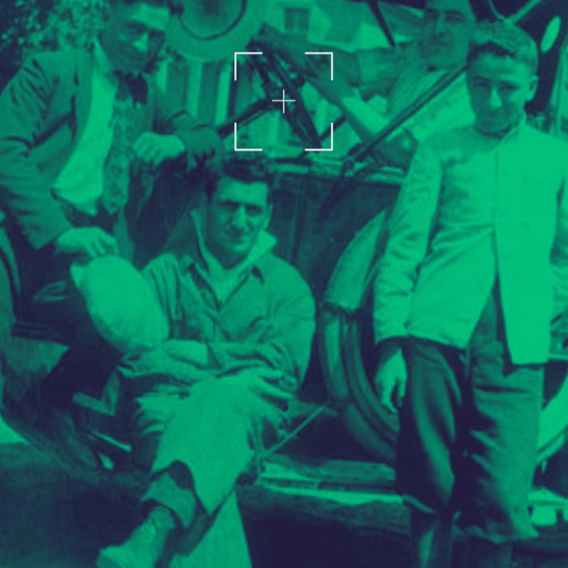 Four young men in vintage clothing pose around an old car, with a green filter applied to the scene.