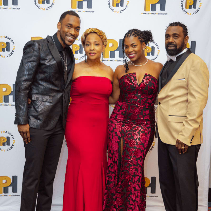 Four elegantly dressed individuals pose for a photo in front of a backdrop featuring the "PHAROAH FAMILY FOUNDATION" logo.