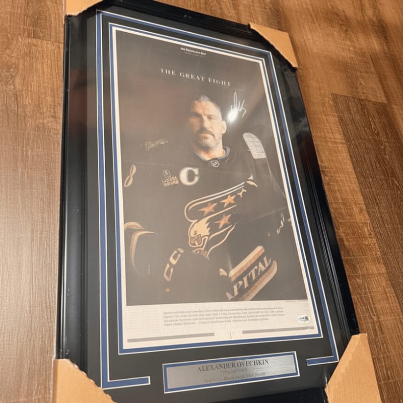 A framed portrait of hockey player Alexander Ovechkin is displayed on a wooden floor, with cardboard packaging surrounding it.