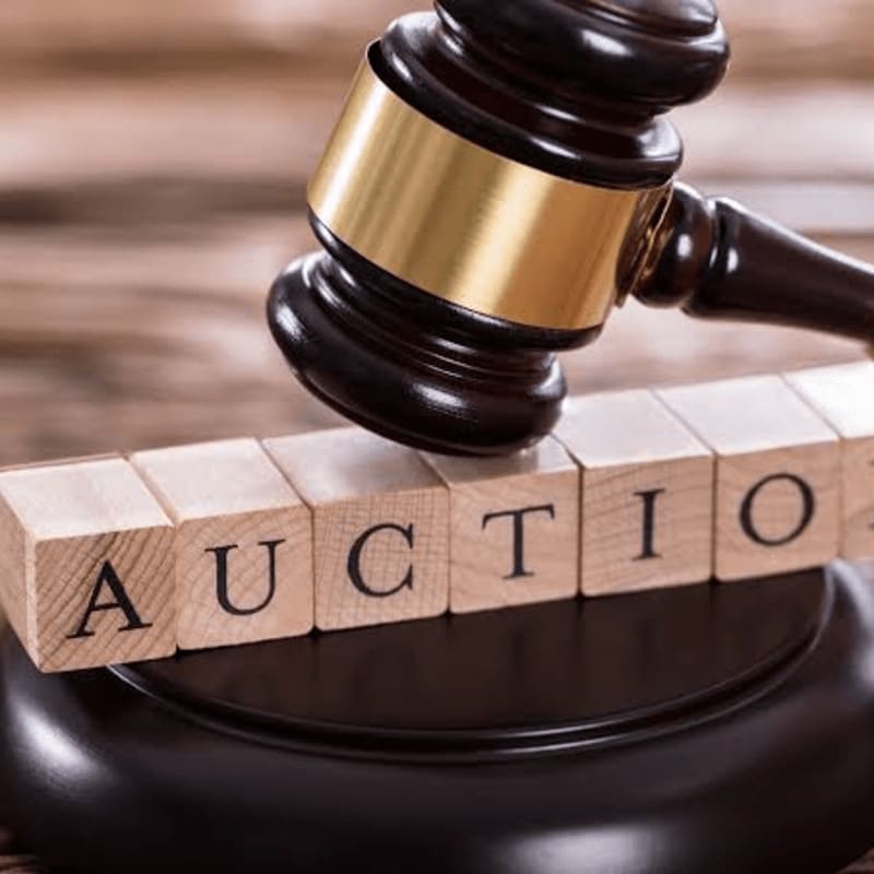 A gavel rests on wooden blocks spelling "AUCTION" against a blurred wooden background.
