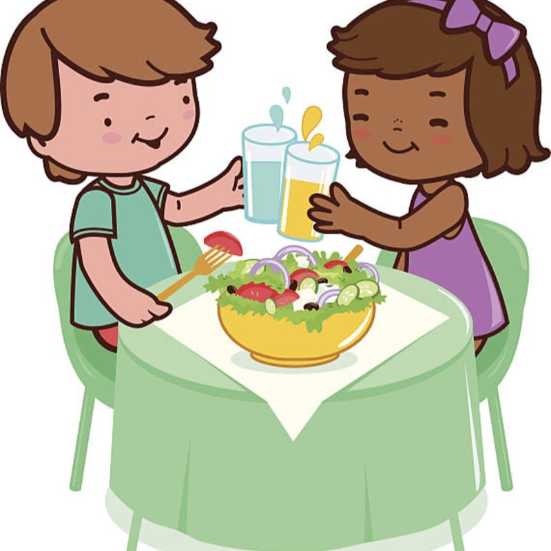 Two children clink glasses of juice over a bowl of salad on a table with a green tablecloth.