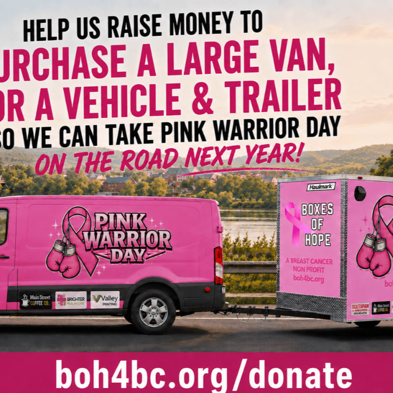 A pink van and trailer, emblazoned with "Pink Warrior Day" and "Boxes of Hope," are parked by a river with trees and hills in the background.
