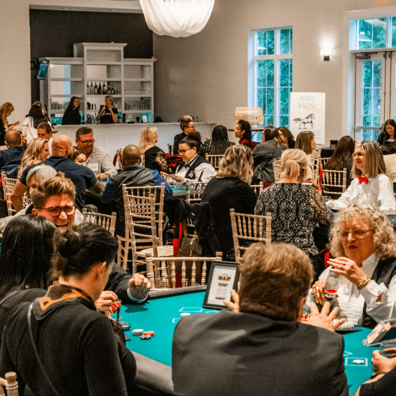 People are playing poker at tables in the foreground, while a bar and large windows are visible in the background.