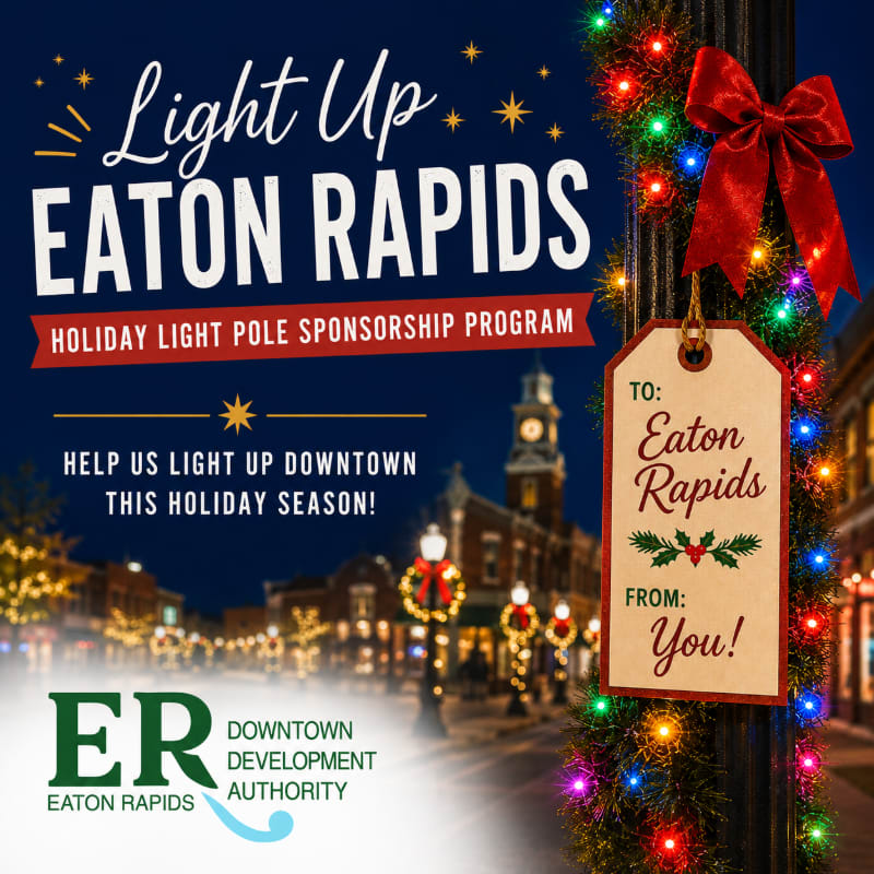 A festive holiday scene in Eaton Rapids features a light-adorned lamppost with a gift tag in the foreground and a decorated downtown street in the background.