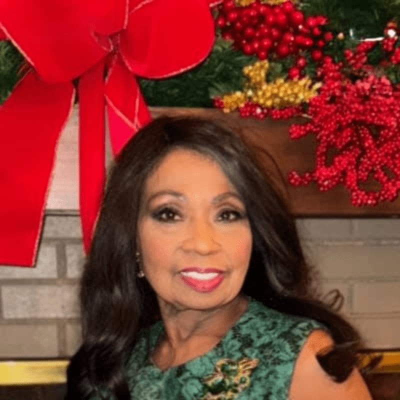A smiling woman in a green dress is in the foreground, with a festive Christmas wreath and red bow in the background.