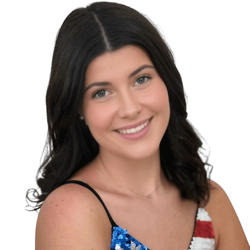 A smiling woman with dark hair wears a sequined top with an American flag pattern against a plain white background.