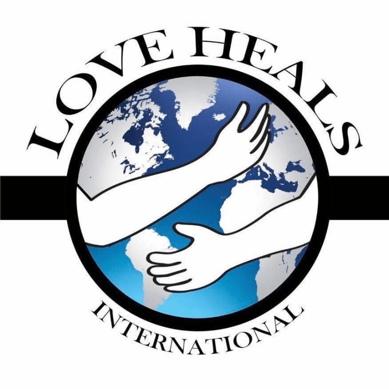 Two arms embrace a globe with the words "LOVE HEALS INTERNATIONAL" encircling it.
