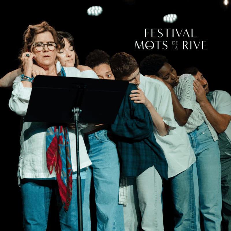 A group of people in casual clothing huddle together behind a music stand in front of a black background with festival text.