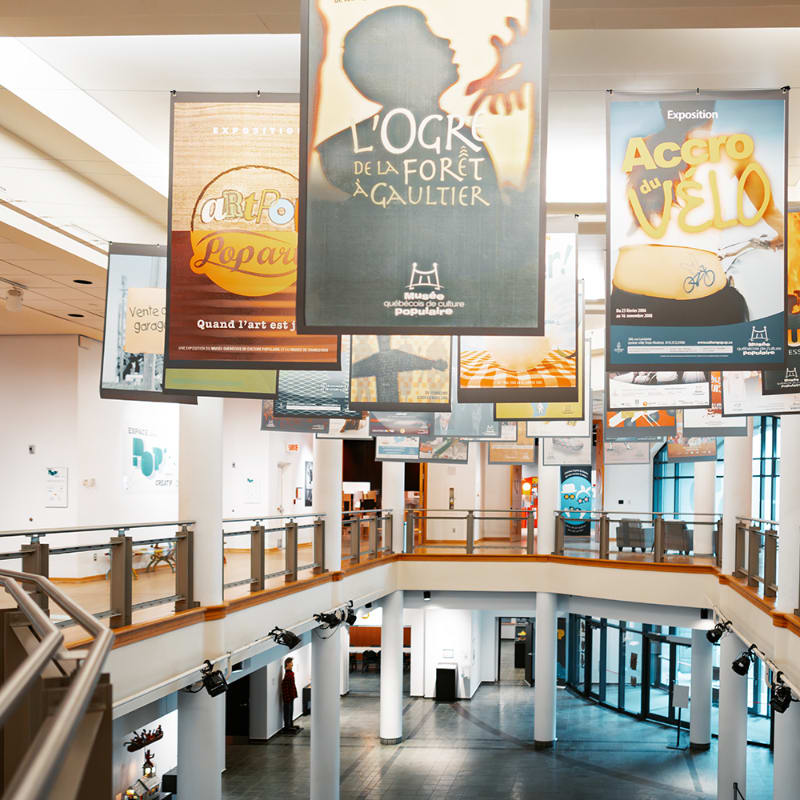 Large posters hang from the ceiling of a multi-level building with a staircase in the foreground and an open atrium in the background.