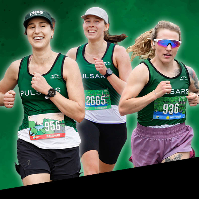 Three women in green running tops with bib numbers are racing forward against a blurred green background.