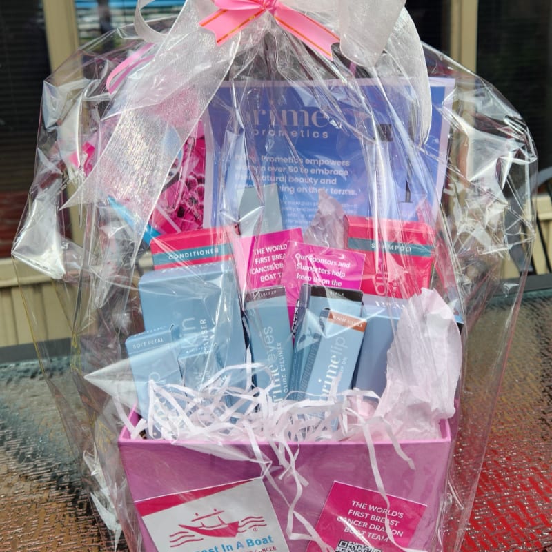 A pink gift basket filled with beauty products is wrapped in cellophane and tied with a pink bow, with a blurred outdoor background.