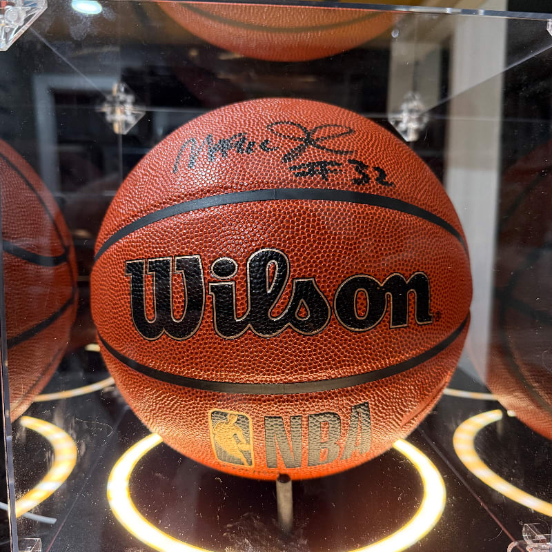 A signed Wilson NBA basketball sits in the foreground within a display case, with other basketballs visible in the blurred background.