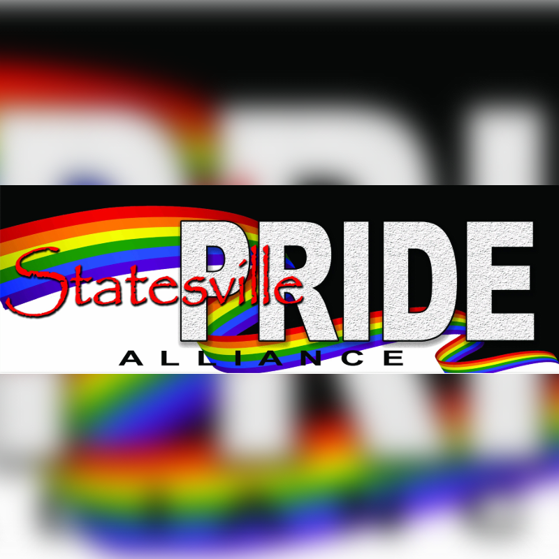 A rainbow-colored banner with "Statesville PRIDE ALLIANCE" written on it is blurred in the foreground, with a more intensely blurred rainbow pattern in the background.