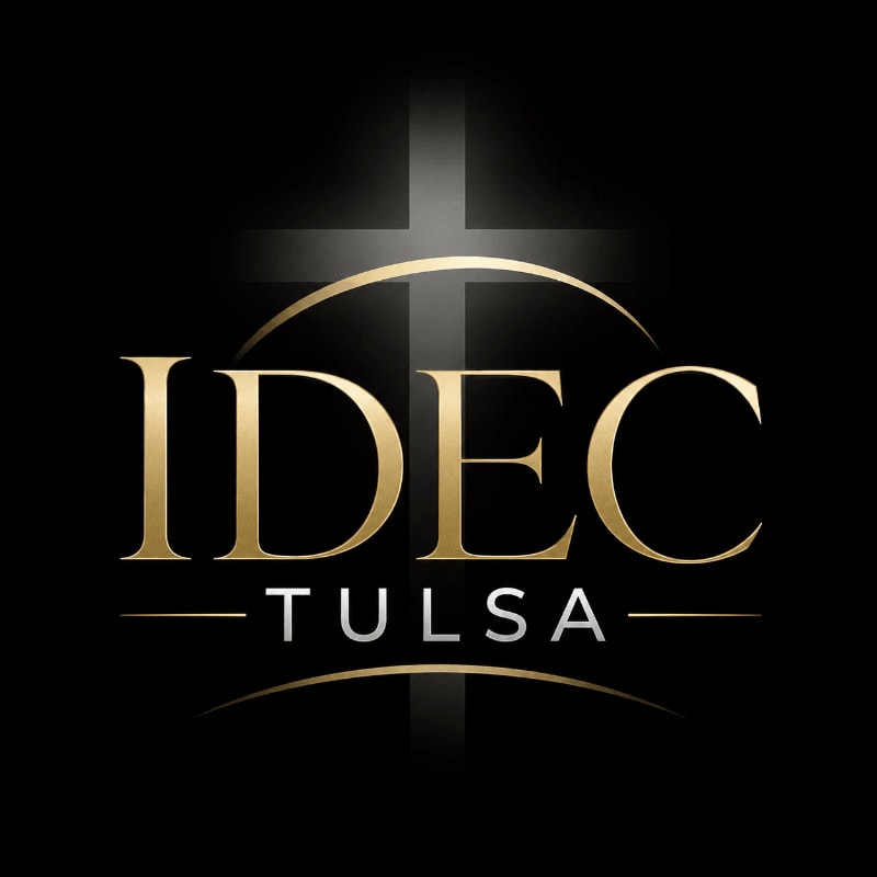 Golden letters spelling "IDEC TULSA" are centered in the foreground against a black background, with a subtle cross design illuminated behind them.