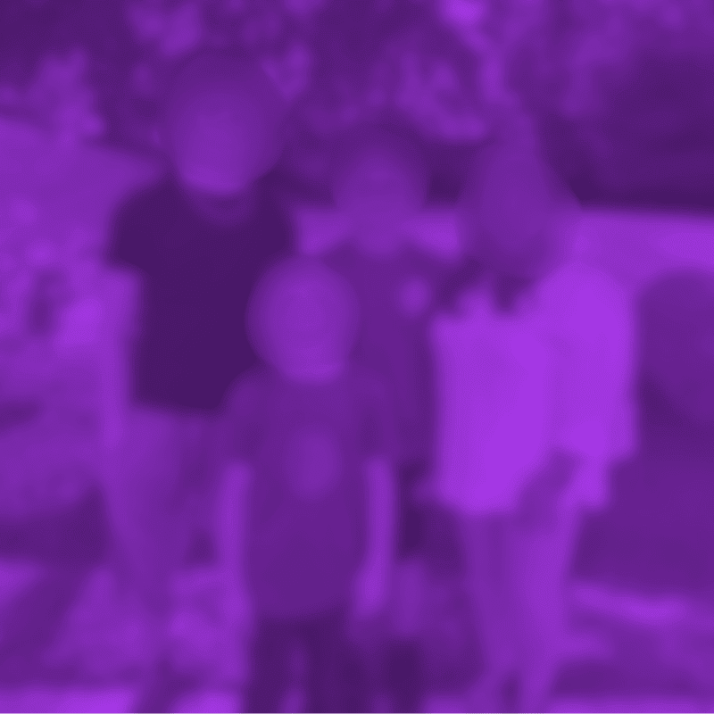 Four blurred figures stand in the foreground against a softly focused, leafy background.
