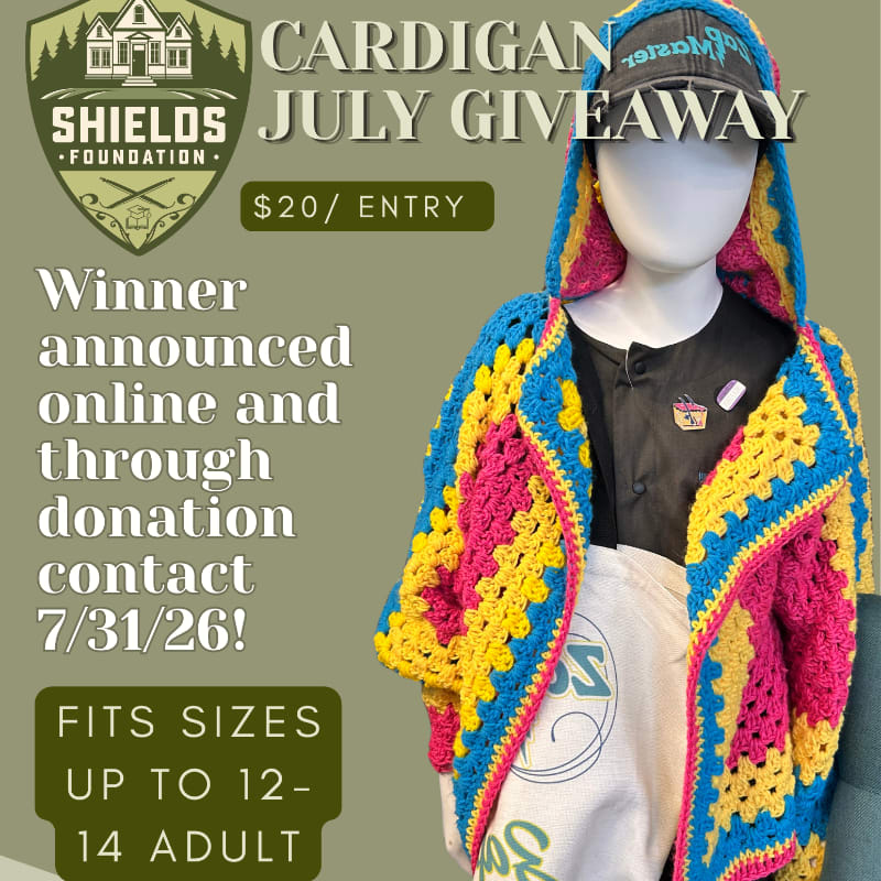 A colorful crocheted cardigan is displayed on a mannequin in the foreground, with promotional text for a July giveaway by the Shields Foundation in the background.