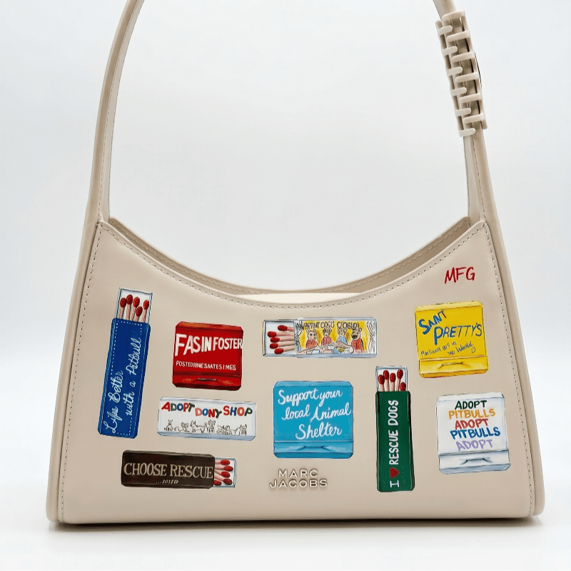 A cream-colored shoulder bag with various patches and designs is displayed against a plain white background.