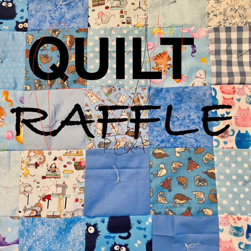 A colorful quilt with "QUILT RAFFLE" written across it is displayed against a background of various fabric squares featuring cats and other patterns.